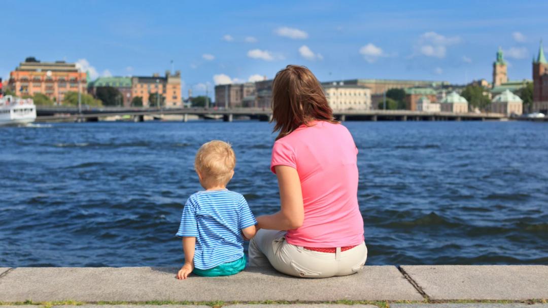 Mamma och barn sitter vid kajkant i Stockholm